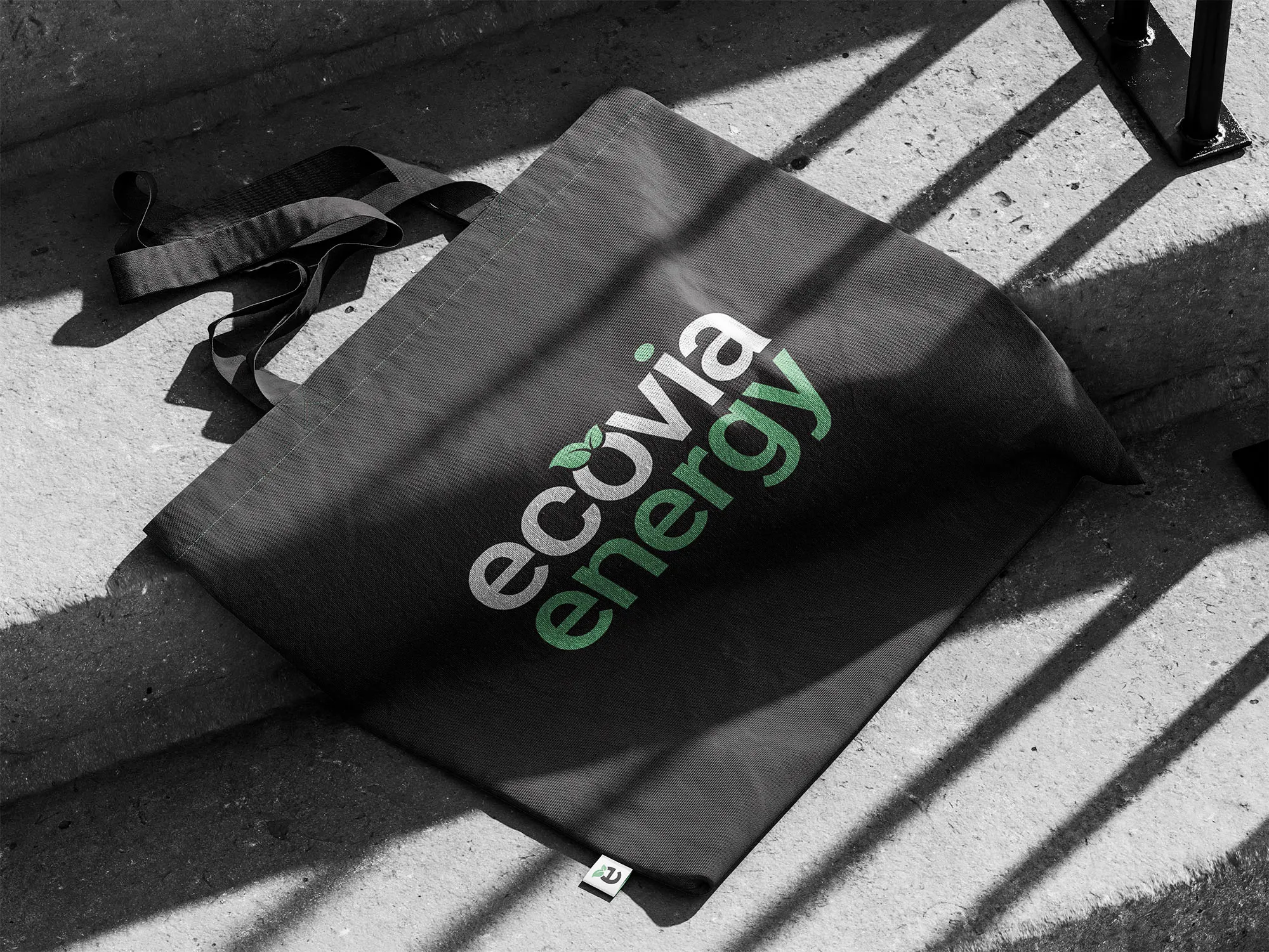 Black tote bag printed with the white-and-green Ecovia Energy logo in sunlight.