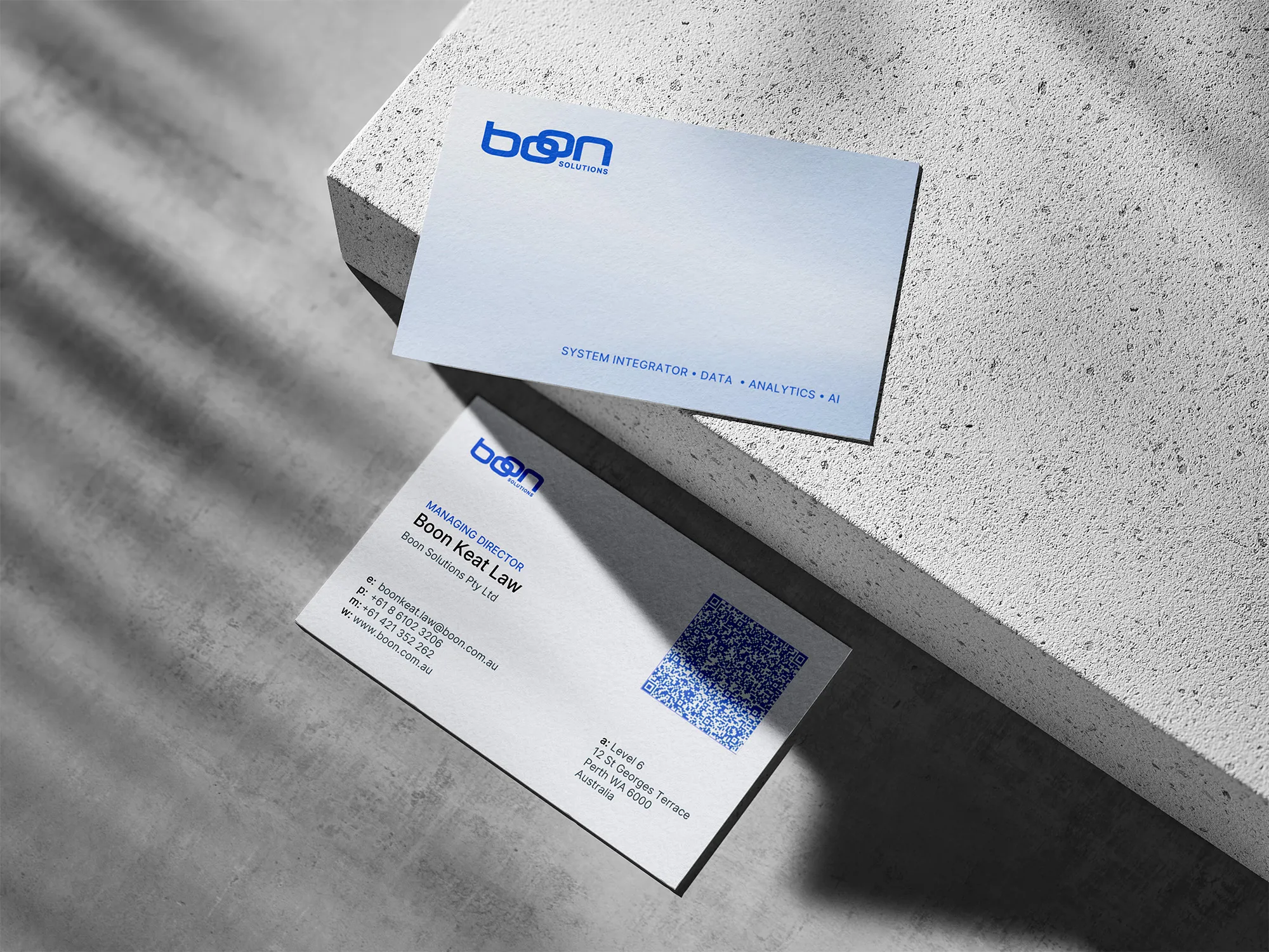 Boon Solutions business cards with blue branding displayed on a sunlit concrete surface.