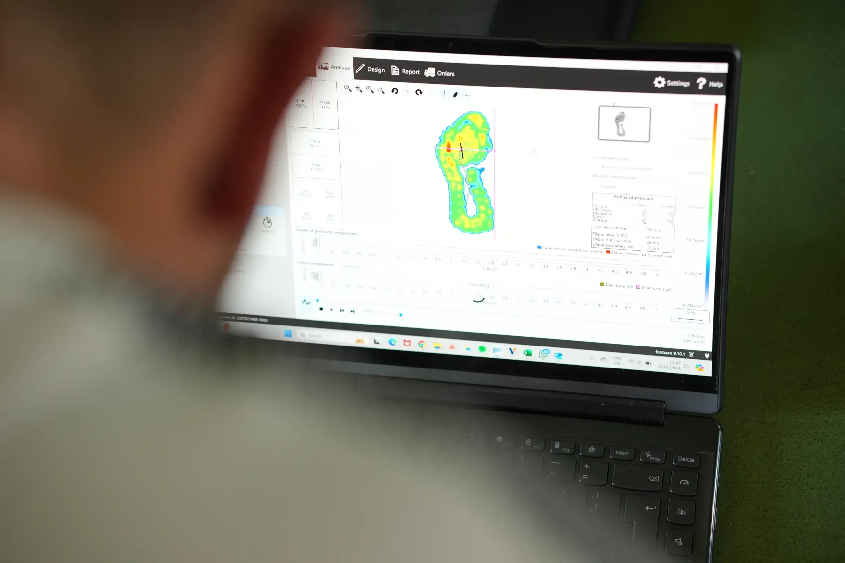 Person viewing a laptop screen displaying a colorful footprint pressure analysis with data charts and settings.