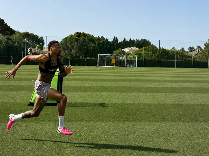 Athlete sprinting on grass field near soccer goal and training dummy under clear sky.
