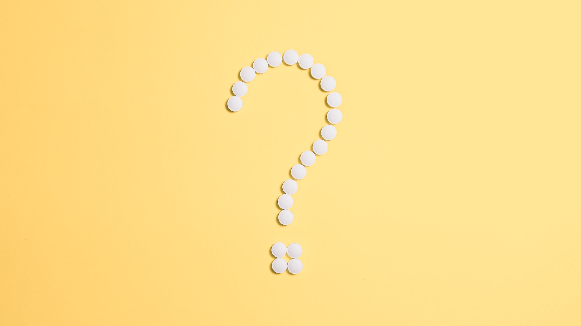 pills in the shape of a question mark on a yellow background