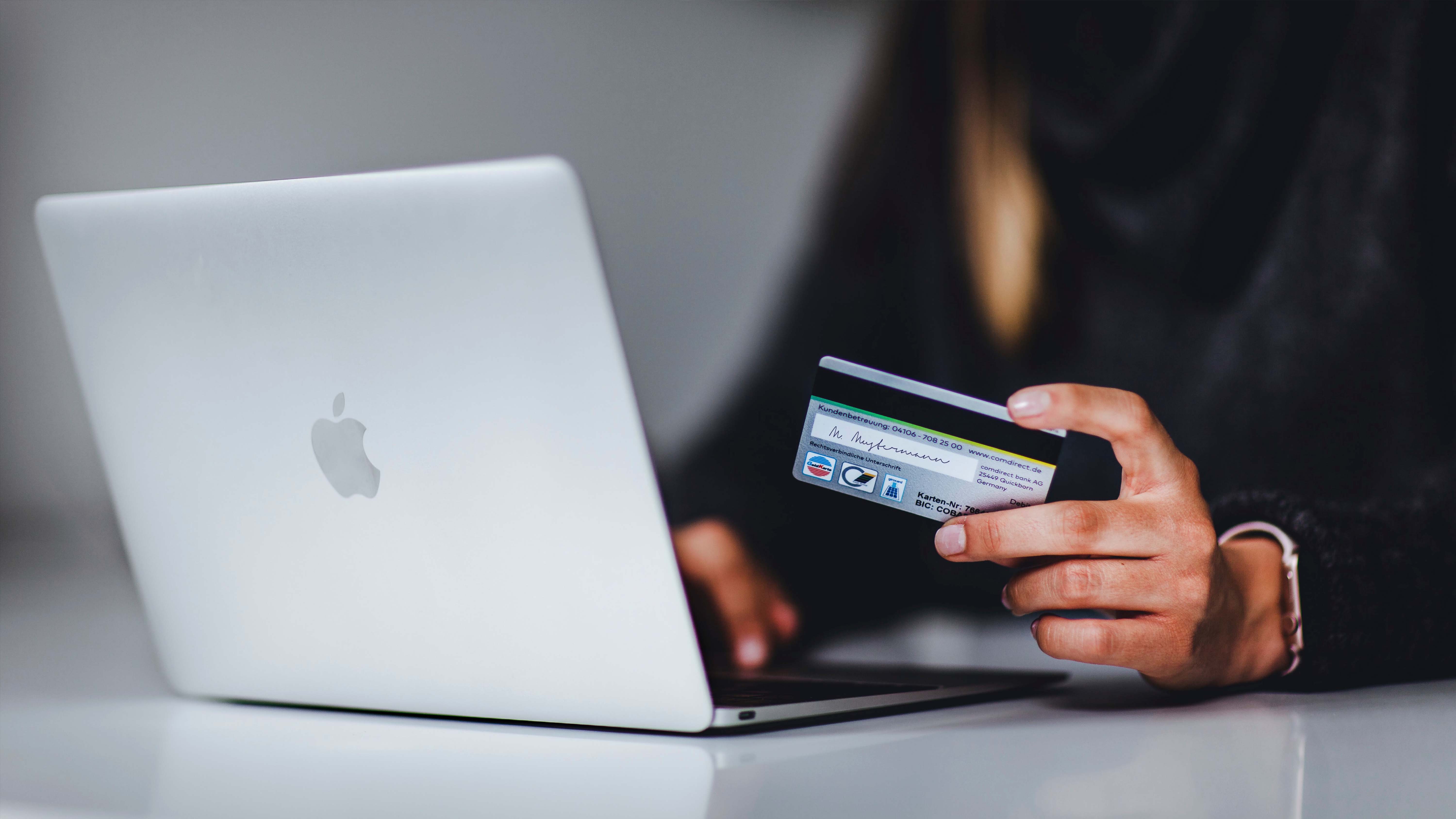 A person holding a credit card while typing on a laptop