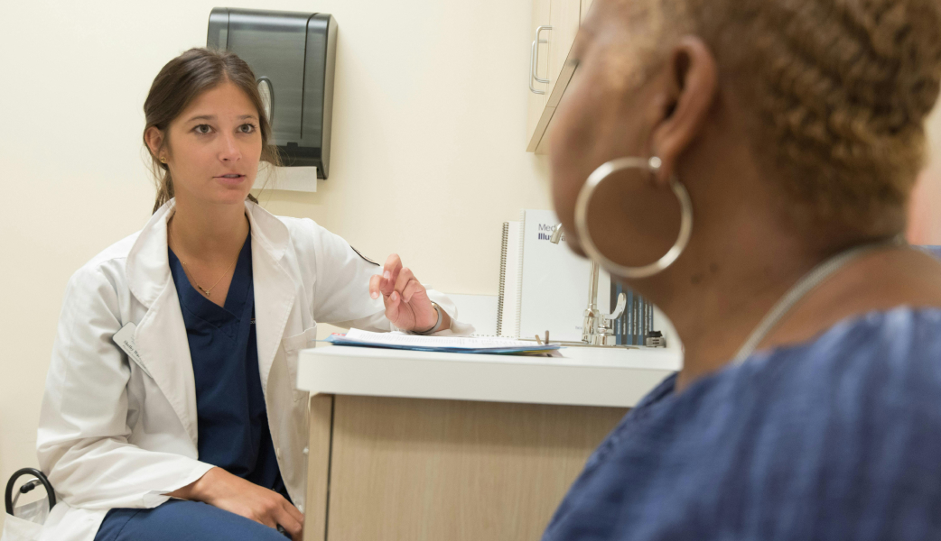 Female healthcare staff in a white coat speaking to a female patient
