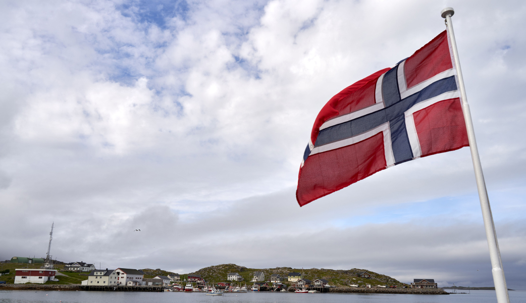 norwegian flag in the foreground and a costal strip or norway in the background