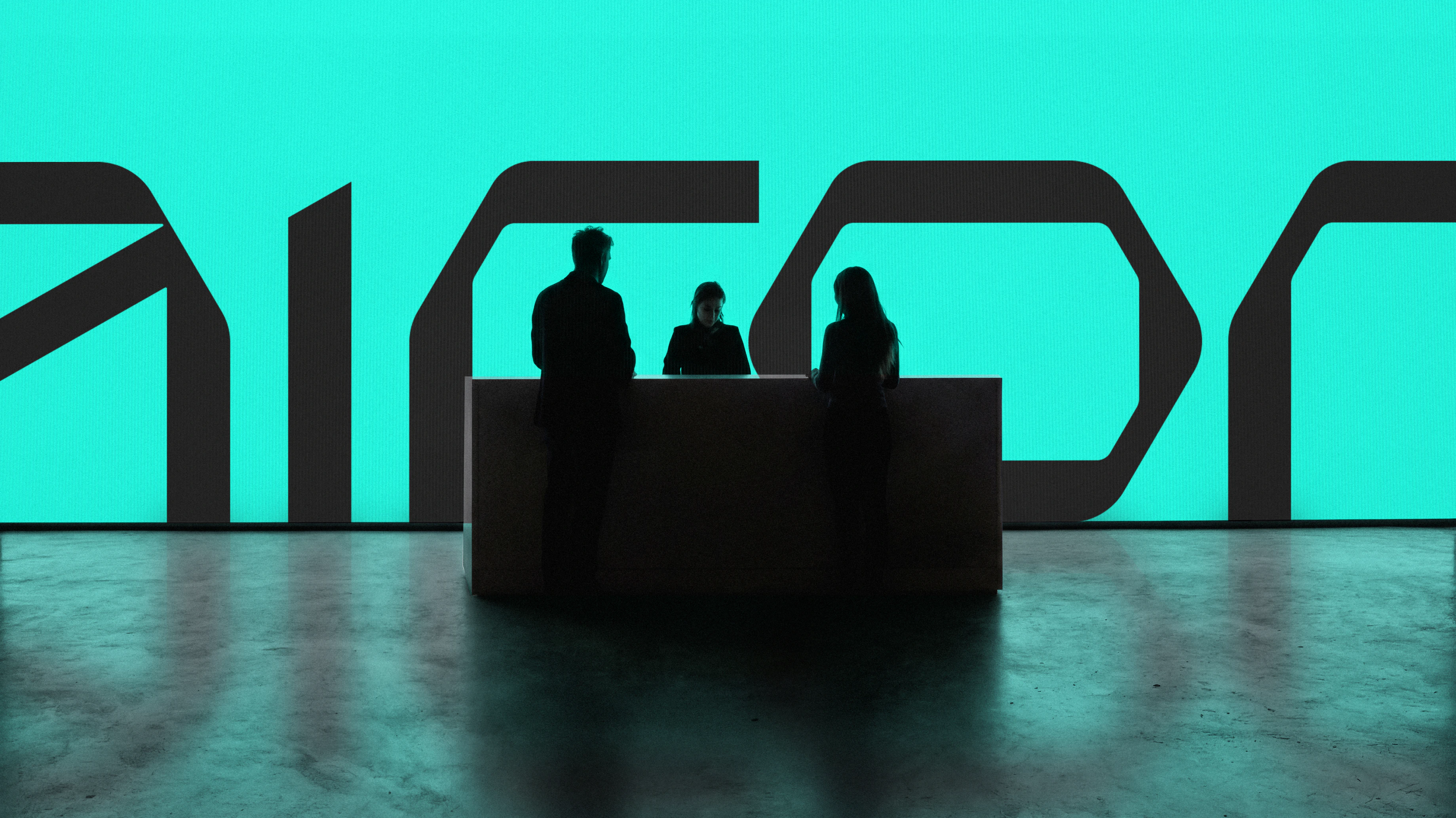 Silhouetted people at a reception desk against an oversized Airon logotype on a turquoise wall.
