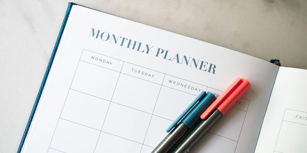 Open monthly planner with blank weekly grid and two felt-tip pens