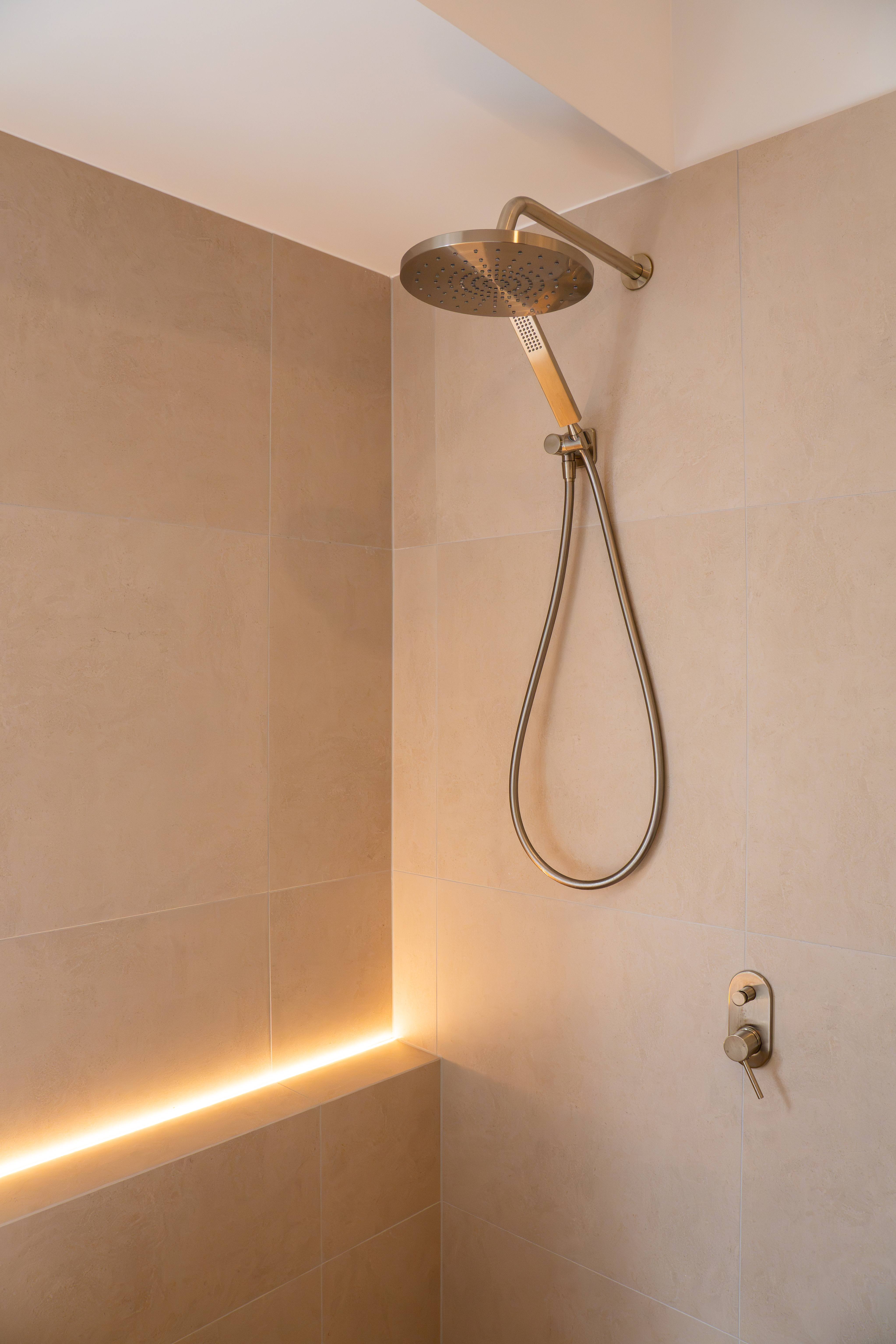 Walk-in shower with brushed fixtures and concealed lighting along the shower ledge