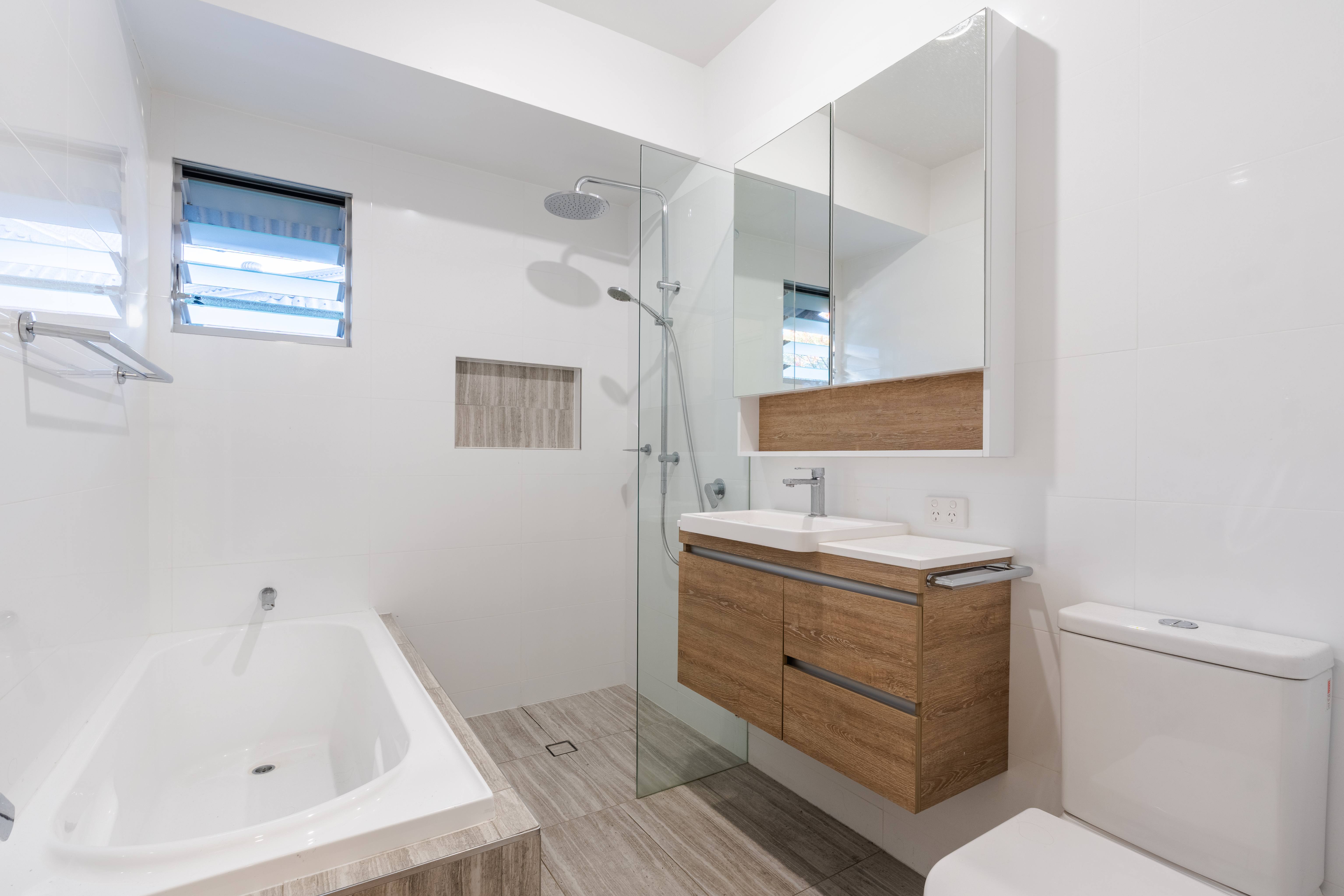 The original bathroom before renovation, with white tiles, a built-in bath and a timber-look vanity