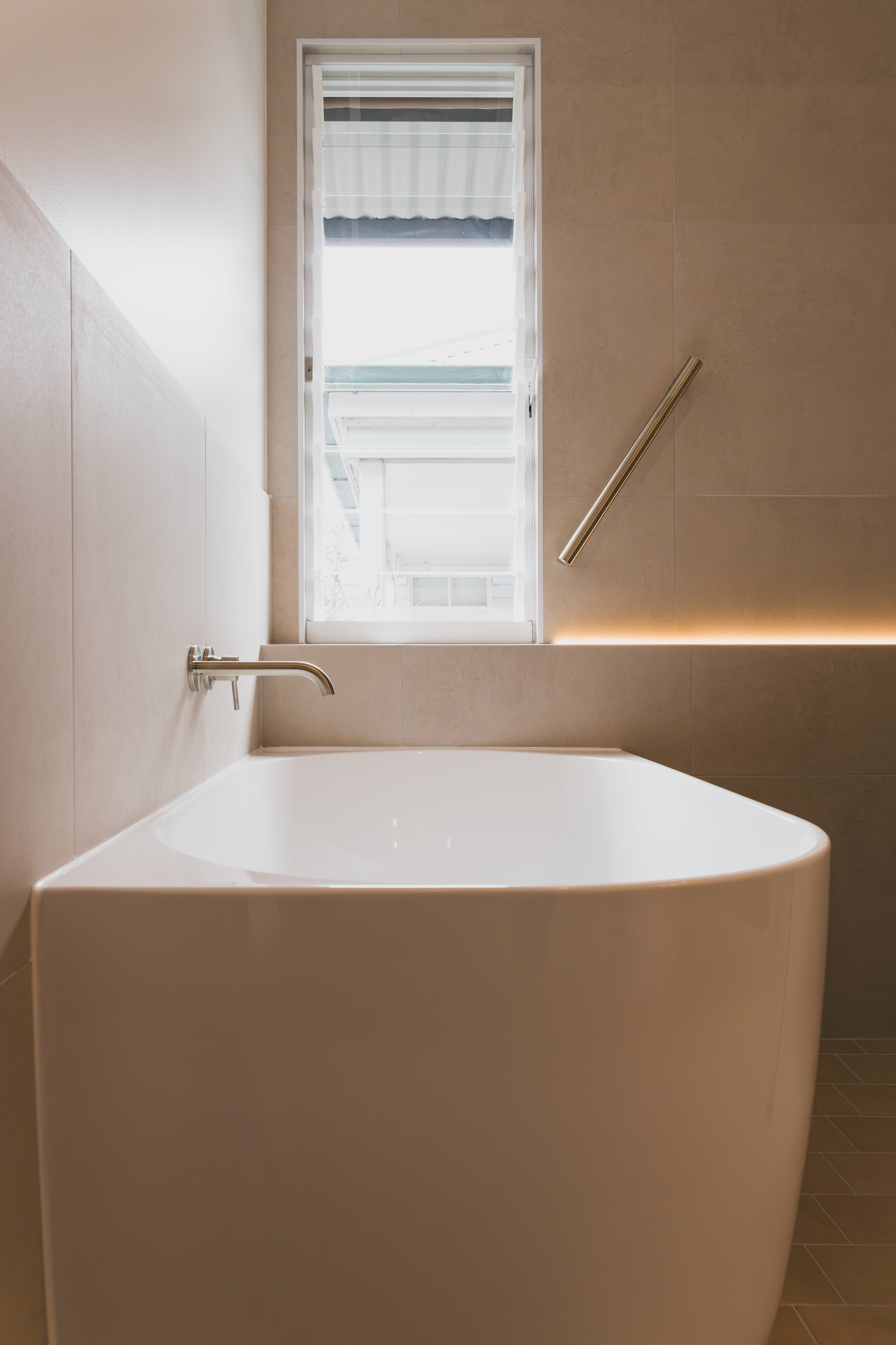 Freestanding bath beneath a tall louvre window with a wall-mounted spout