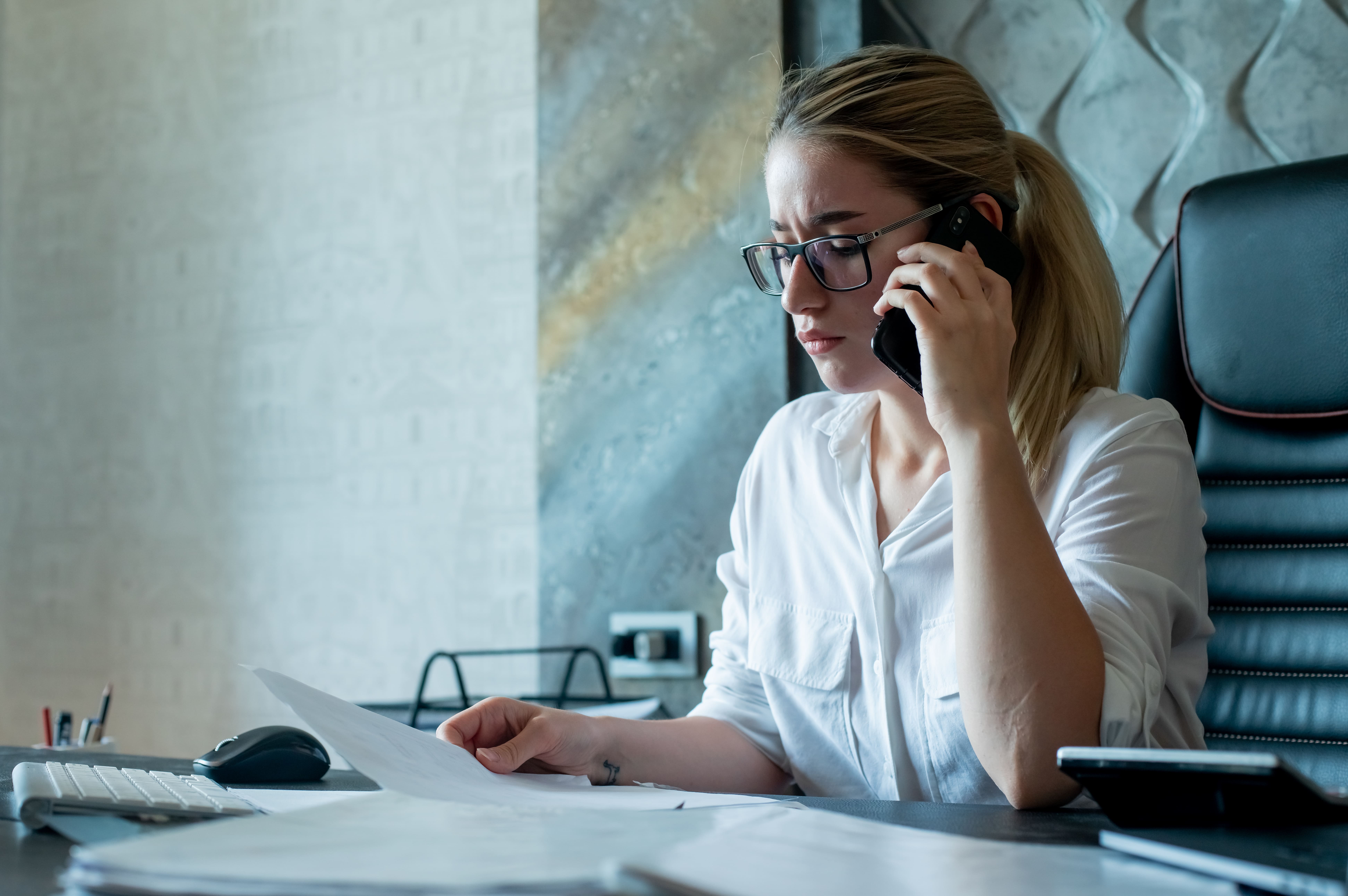 Commerciale au téléphone et analysant des documents, utilisant un logiciel d'enregistrement de vente doté d'intelligence conversationnelle sales et de transcription IA commerciale pour améliorer le ROI enregistrement des ventes.