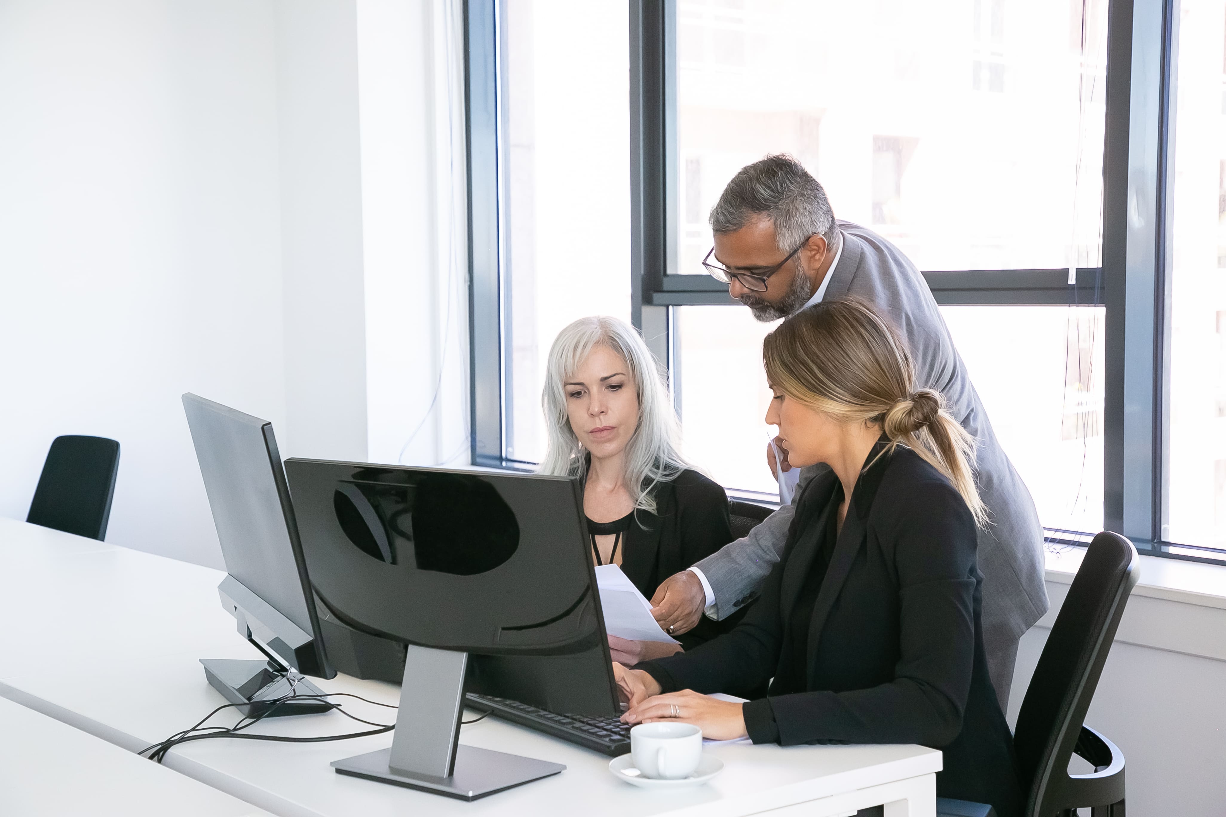 A sales team of three collaborating around a computer, using the Praiz platform to review a complex deal through the MEDDIC sales framework, aiming to boost sales productivity and ensure CRM automation.