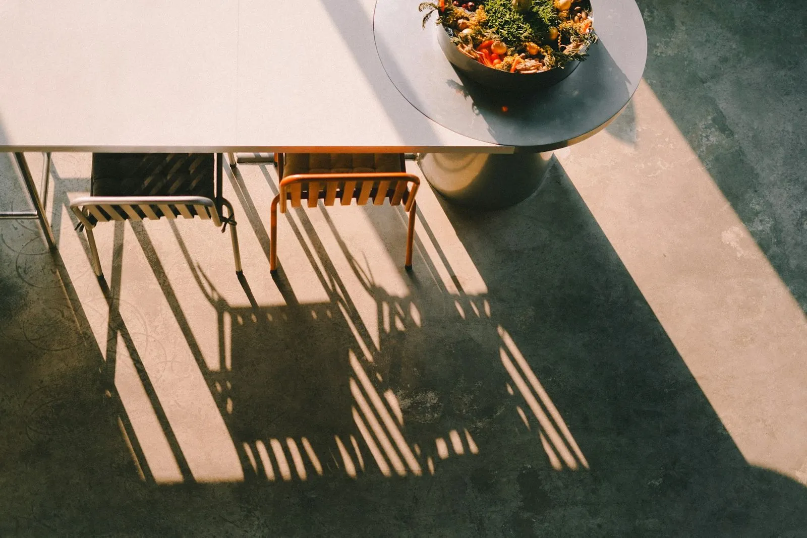 overhead photograph of a white table with two chairs on a concrete floor