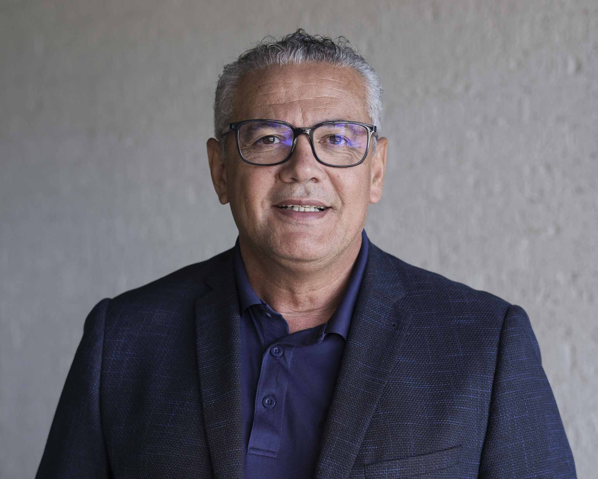 Dr. Ximenes, a Brazilian older male, with blue suit over a polo smiling towards the camera for a photo.