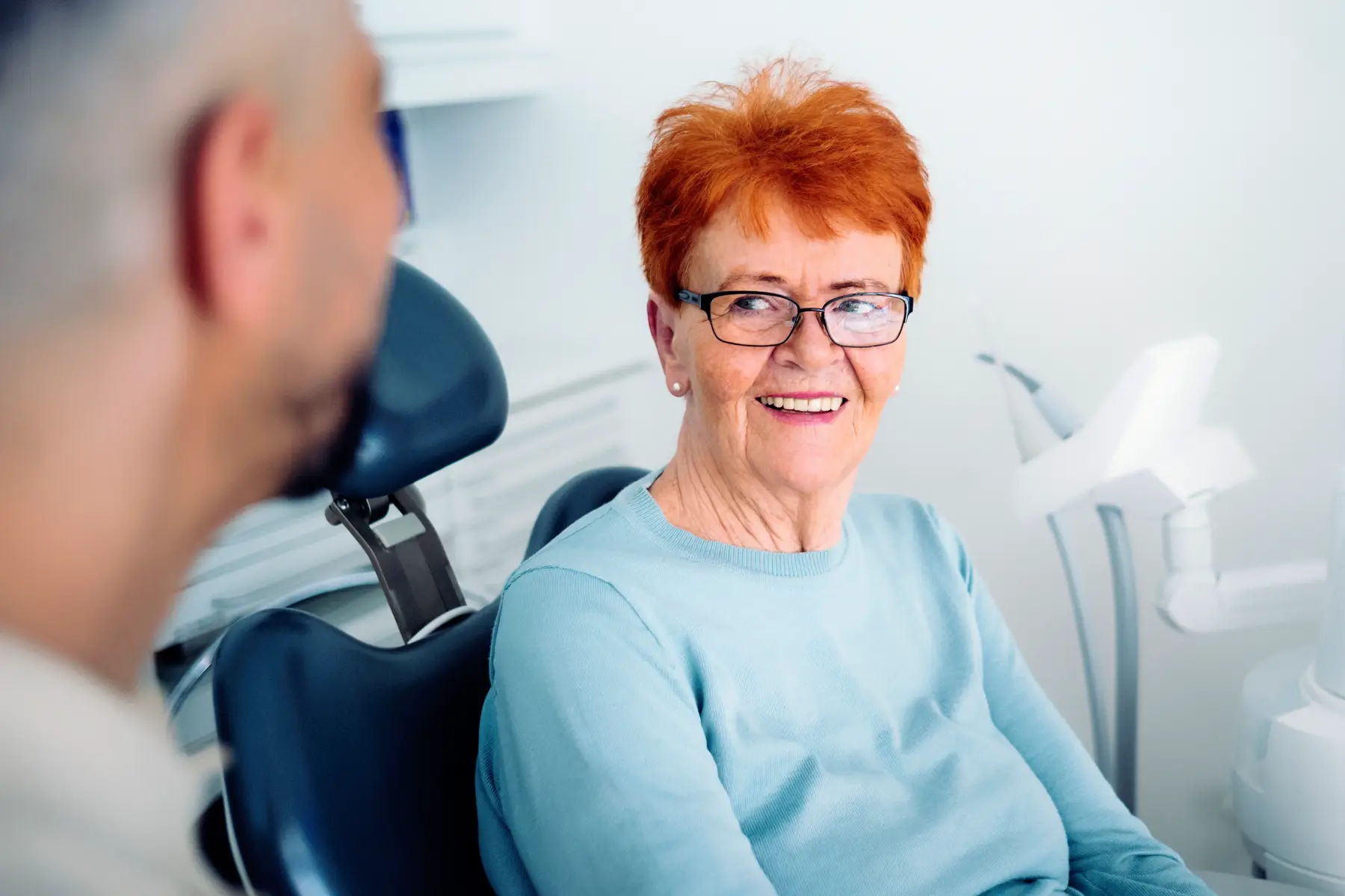 Patient sidder i tandlægestol og kigger på tandlæge