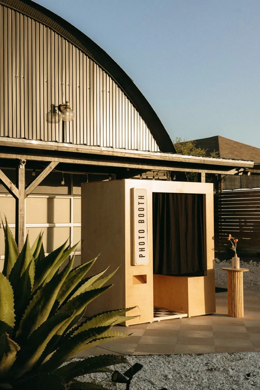 Modern enclosed photo booth rental with agave plant near curved roof building