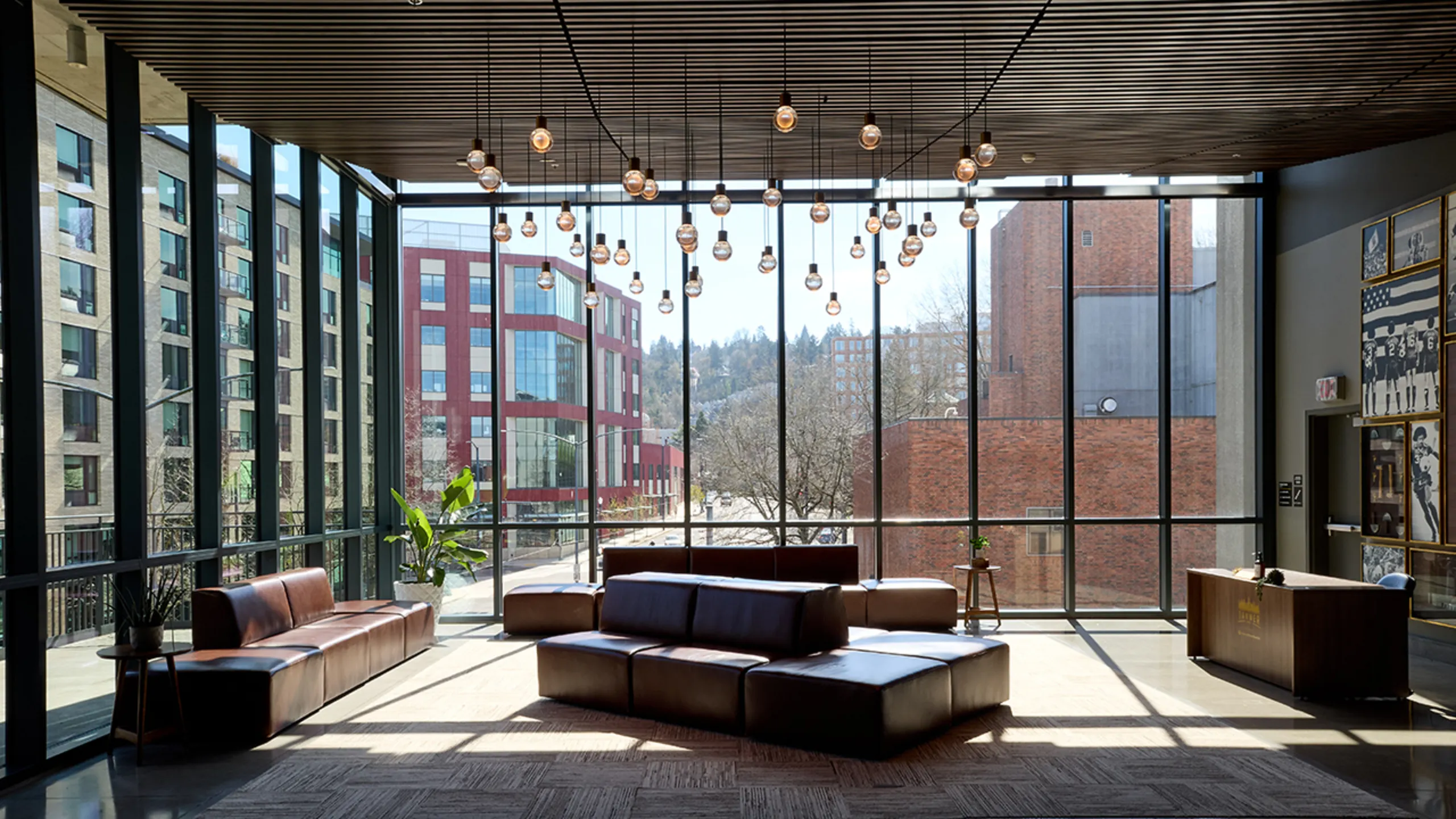 Modern lounge area with leather sofas, hanging light bulbs, large floor-to-ceiling windows, and a wooden reception desk at Providence Park. 