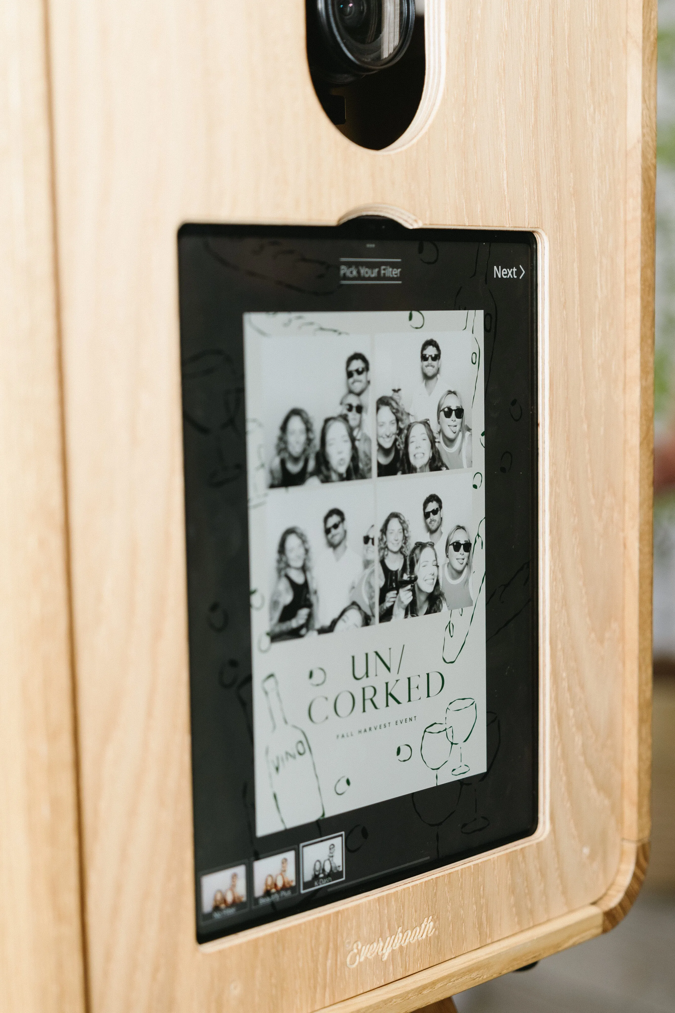 Close-up of a wooden photo booth screen displaying black and white photo strip from an event called Uncorked with four people posing and smiling.