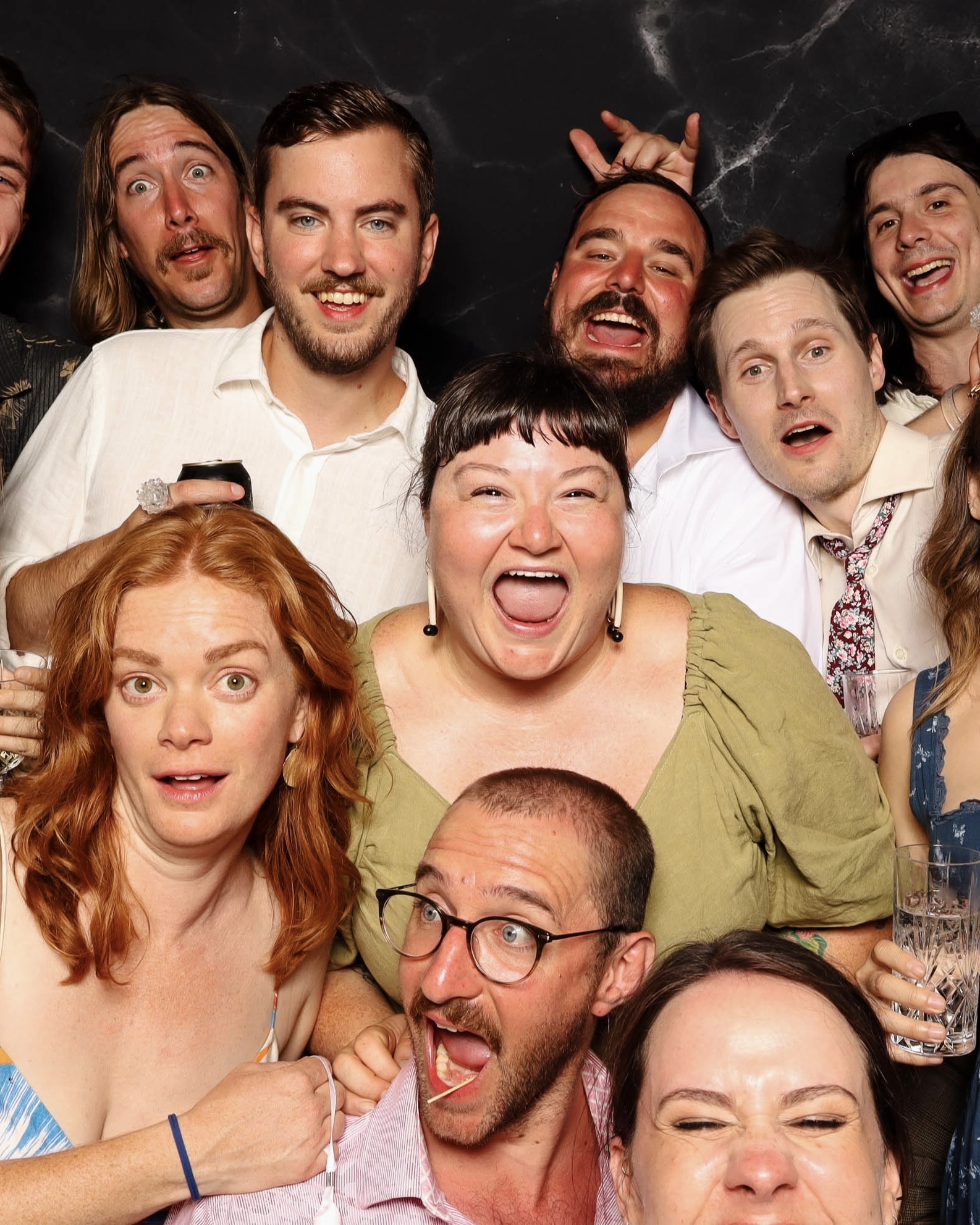 Group of diverse adults smiling and making funny faces in a photo booth with a dark marble backdrop.