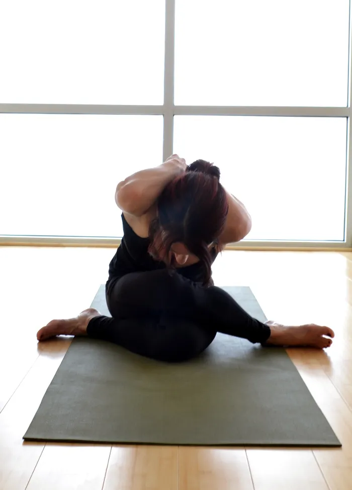 a female in a seated forward bend yin yoga pose on a green mat on a bamboo yoga studio floor