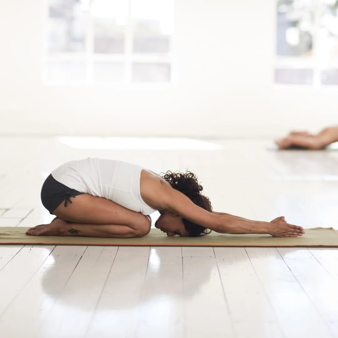 a female in child's pose yoga position on a green mat in a bright yoga studio