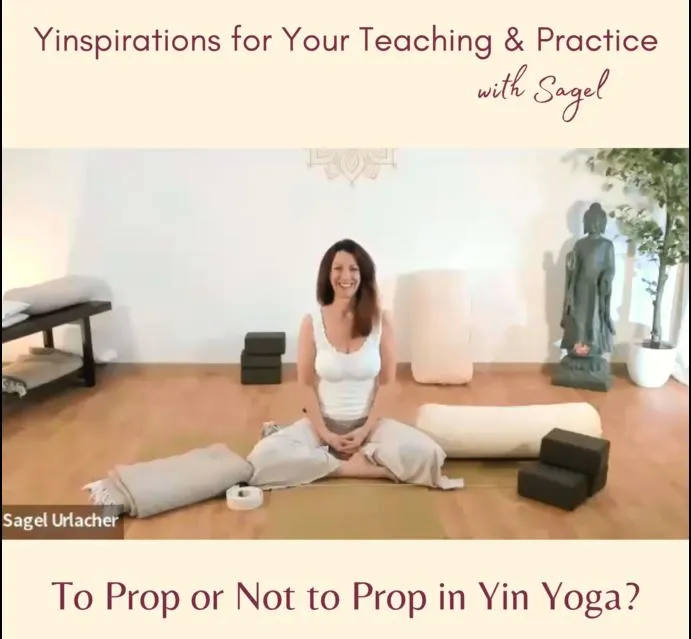 woman sitting cross-legged on a yoga mat surrounded by yoga bolster, blankets, and blocks