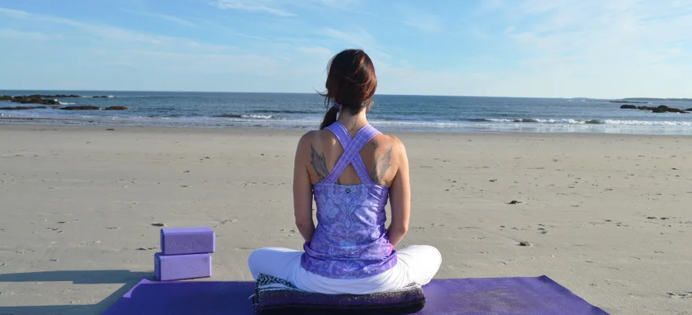 female sitting on a yoga mat on the beach
