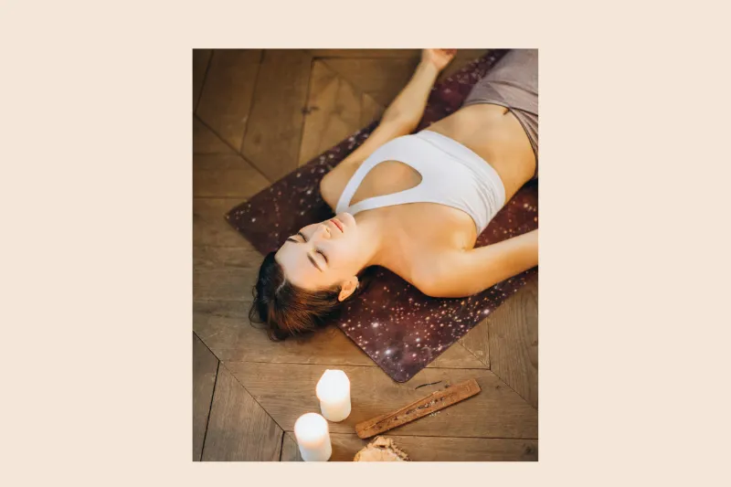 a female yoga student lying peacefully on a yoga mat surrounded by calming candles
