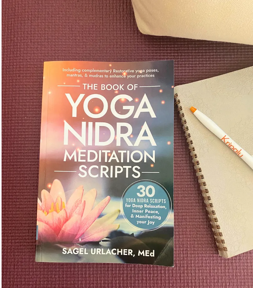 front cover of the Book of Yoga Nidra Meditation Scripts on a turquoise mat with blankets, blocks, and notebook beside it 