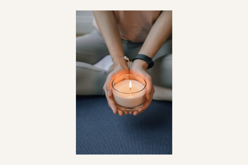 a female yogi sitting on a yoga mat holding a candle