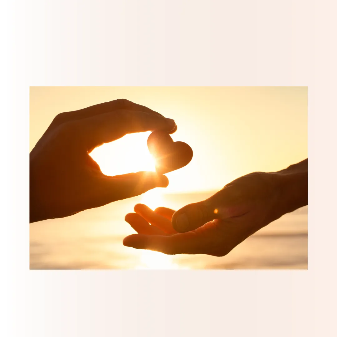 two hands exchanging a red heart in sunshine