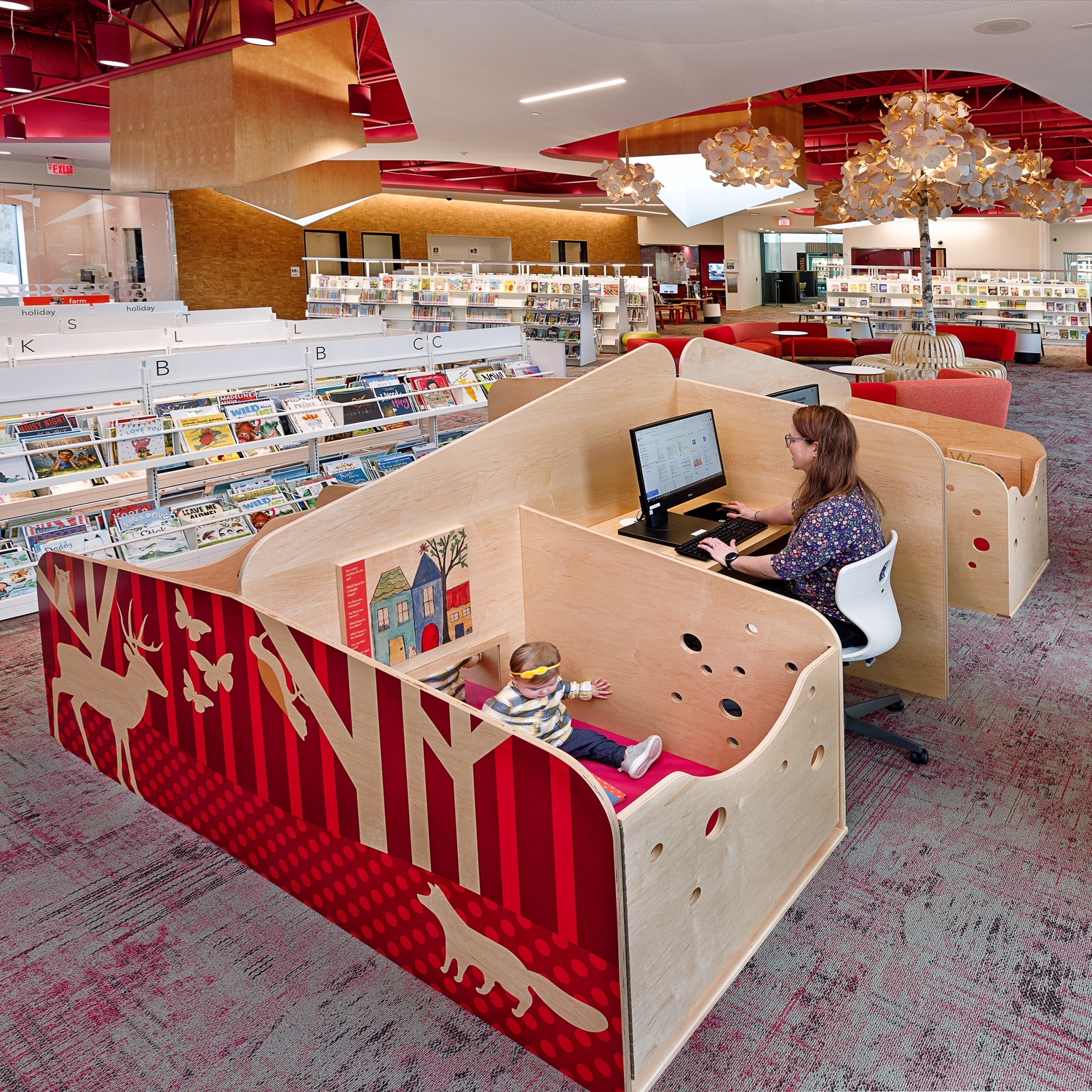 A caregiver uses a library computer in a custom workstation that has an attached play area to keep children secure and entertained.