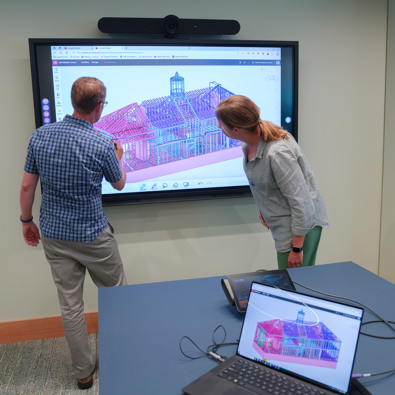 Two team members examine a multi-colored digital twin that is shown on a screen.
