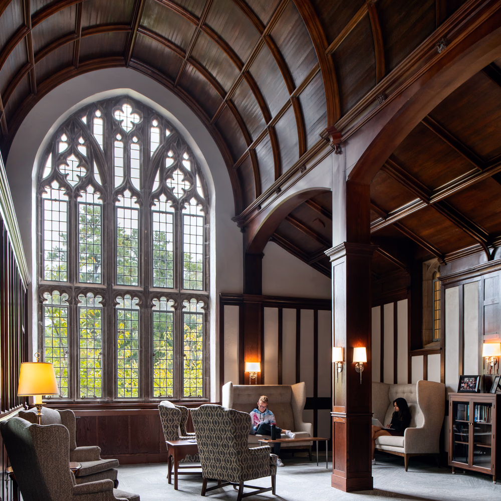 Students read inside the University of Richmond's Humanities Building, near a large arched window with intricate tracery.