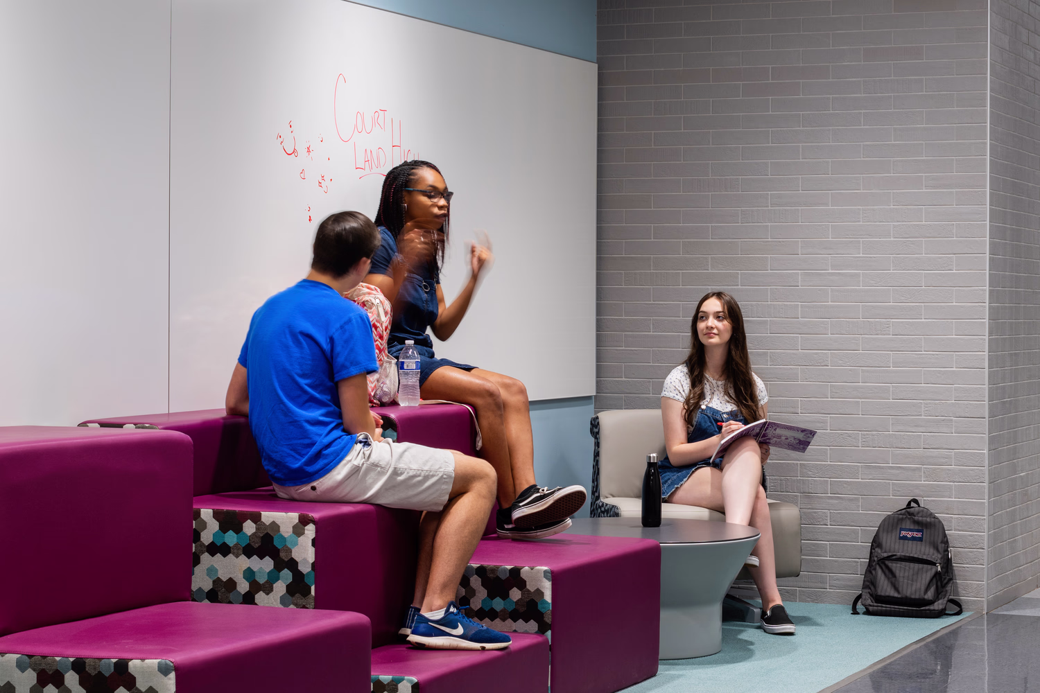 Sitting on large furniture in a nook, students chat inside their school.