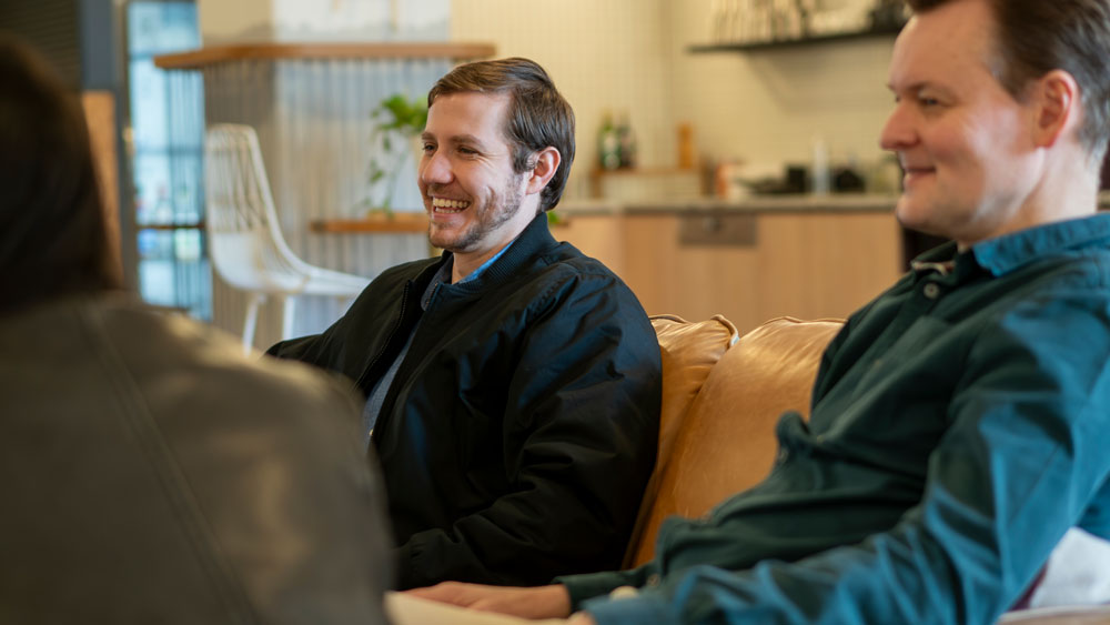 Three people casually sitting and smiling in a modern, comfortable lounge area.