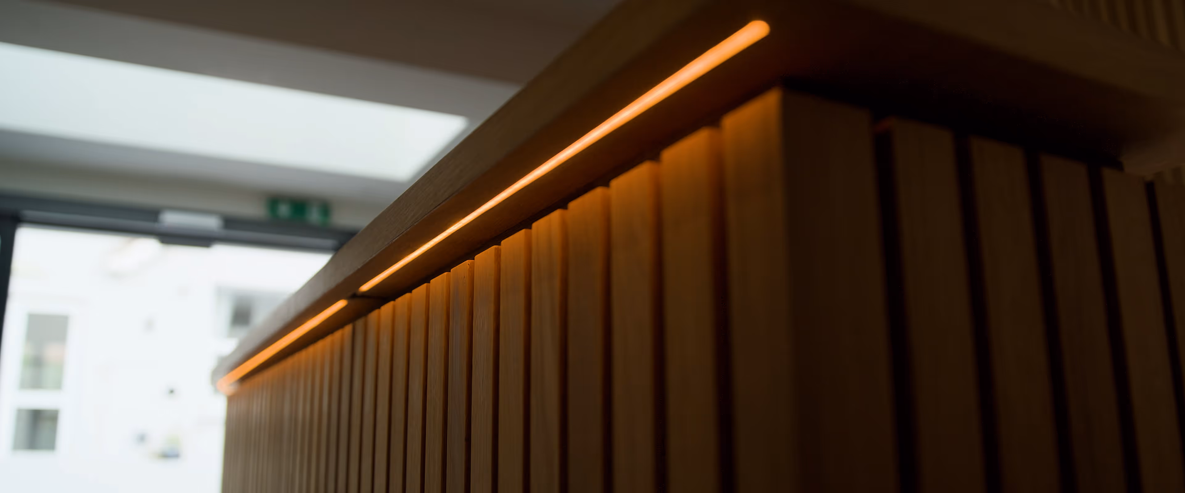 Bespoke curved timber reception desk with vertical slatted panelling and integrated LED lighting in a Seaford care home entrance.