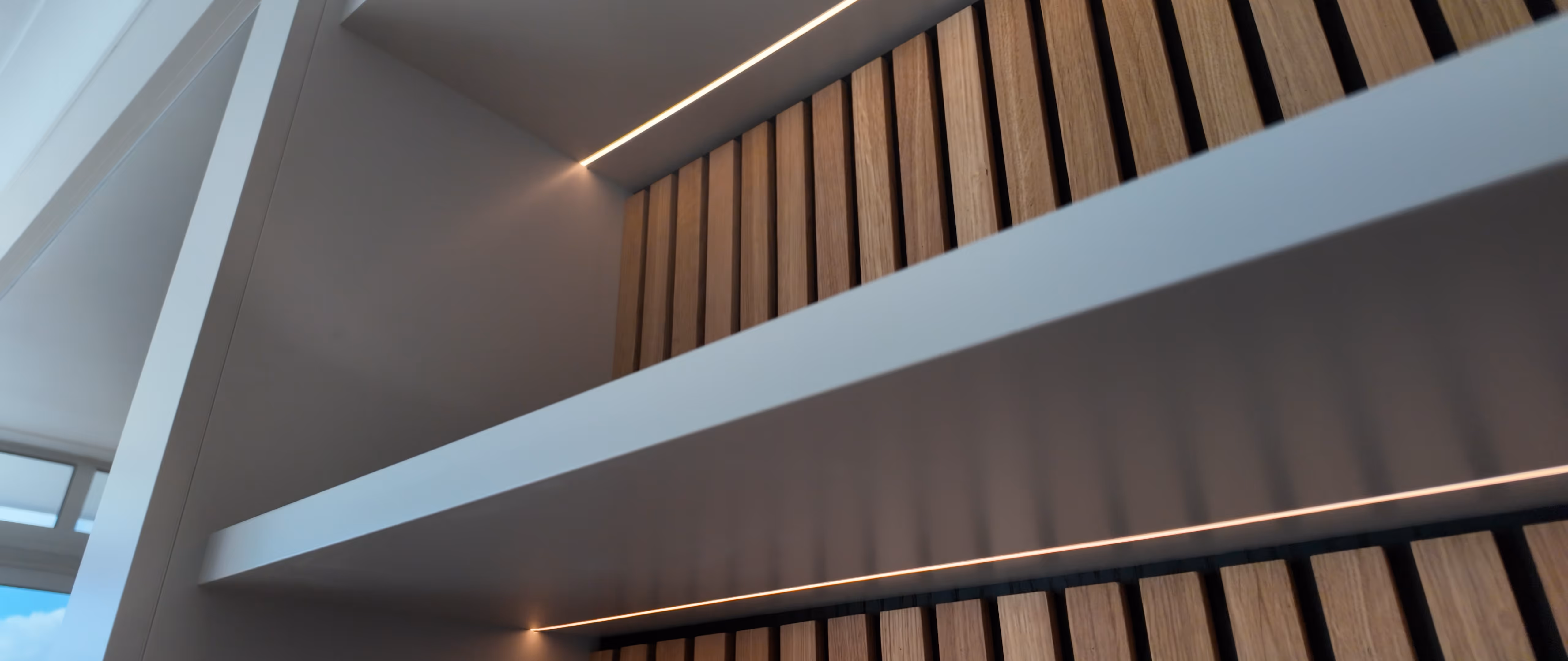 Close-up of bespoke oak slatted wall panelling with integrated linear LED lighting in a contemporary interior feature installation.