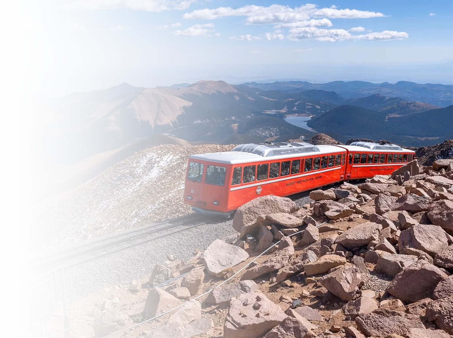 Red scenic railway train ascending a mountain summit with panoramic views of peaks and valleys