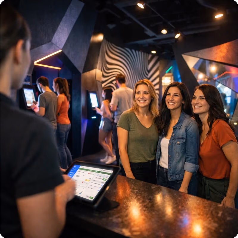 Staff member checking in guests at tablet POS with self-service kiosks in background