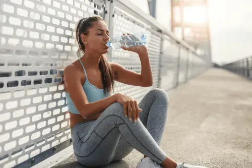 A woman sitting on the ground drinking water.
