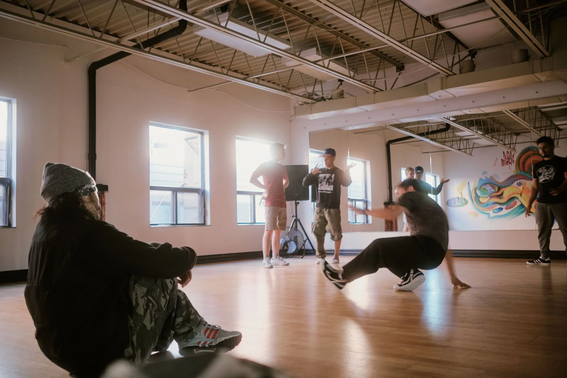 Adult dancers practicing breakdance moves in a sunlit studio with a colourful mural at The Flava Factory.