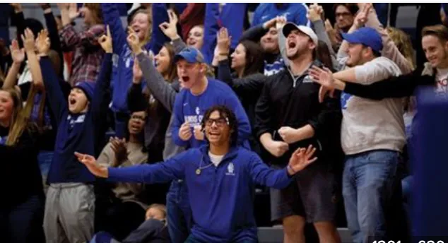 Group of sports fans cheering enthusiastically in stadium stands, wearing blue and white clothing.