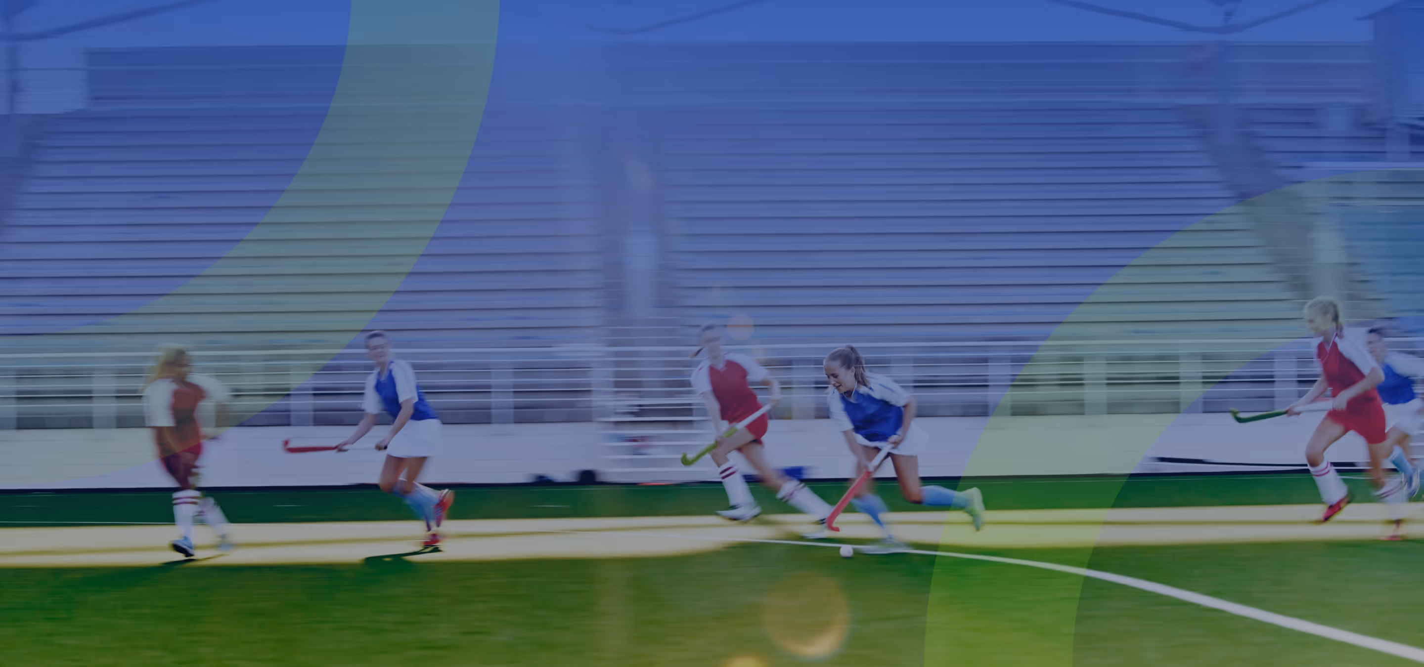 Female field hockey players in red and blue uniforms actively playing on a green field during a match.