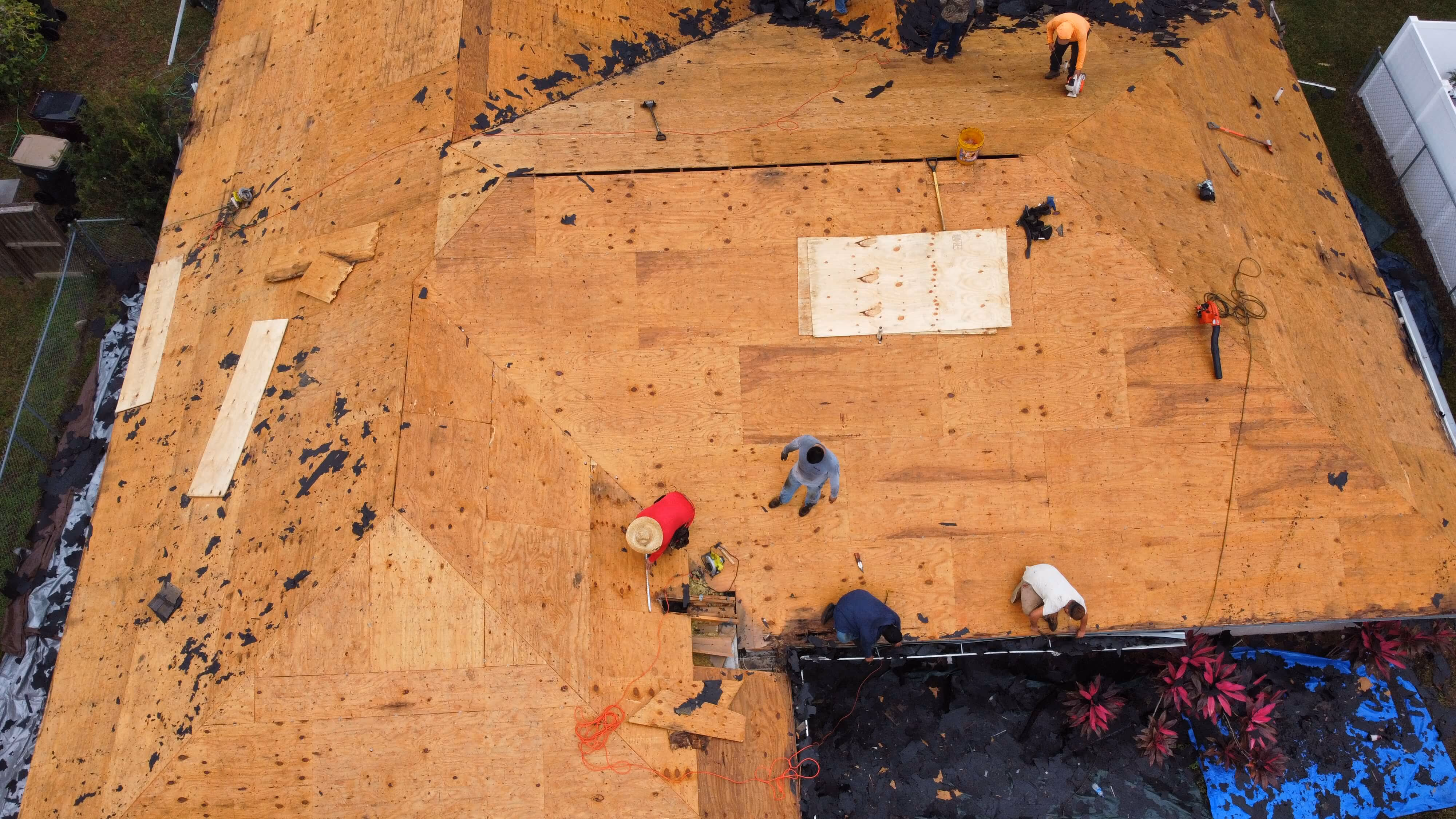 Drone picture of a removed shingle roof down to bare decking and workers on the roof top