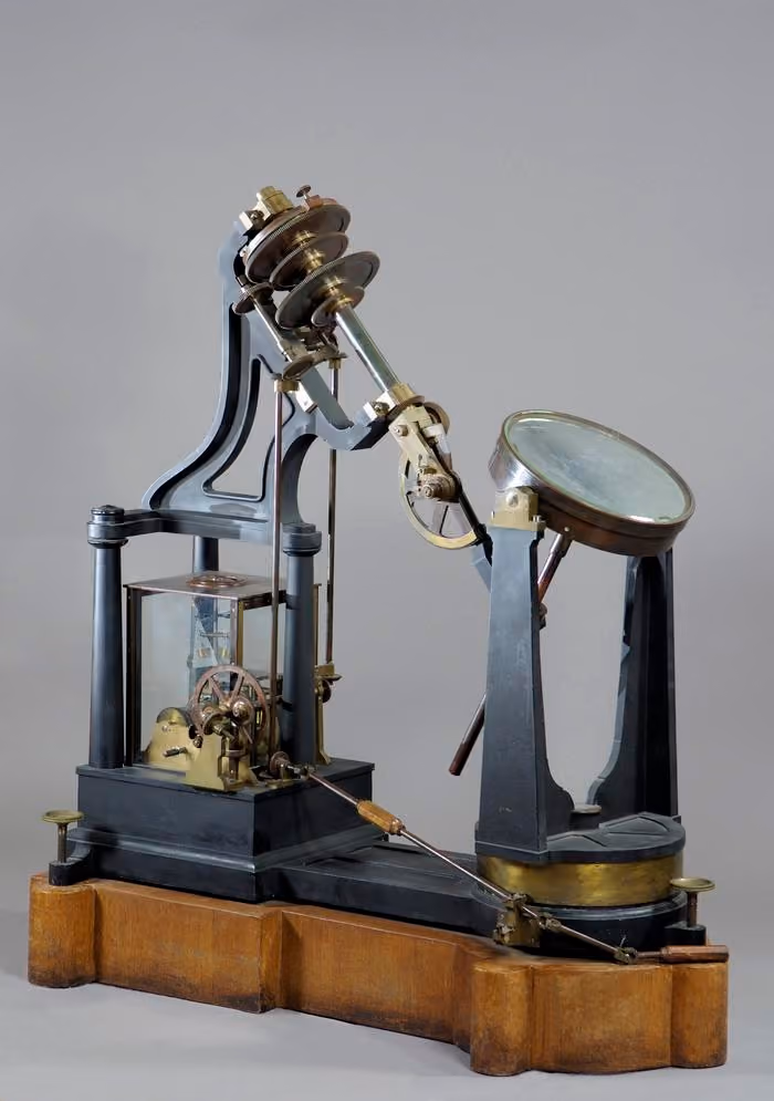 Vintage scientific apparatus with mechanical gears, levers, and a large circular component on a wooden base.