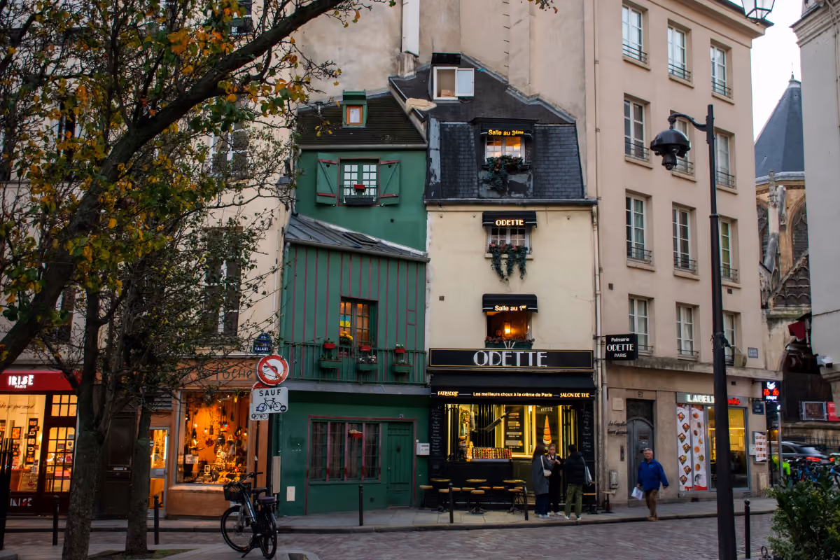 Street view of a green and cream building with Odette bakery and people outside in evening light.