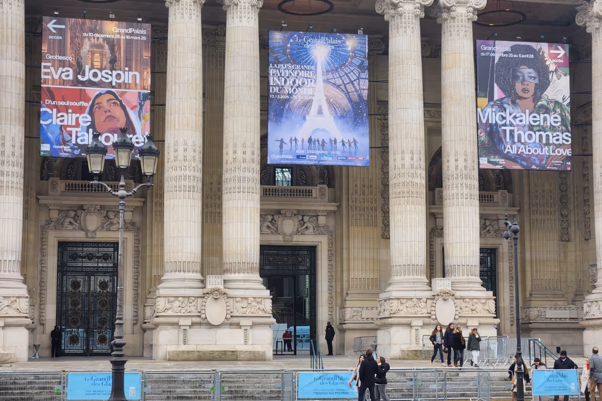 Grand Palais facade with stone columns and three large event banners above entrances and visitors outside.