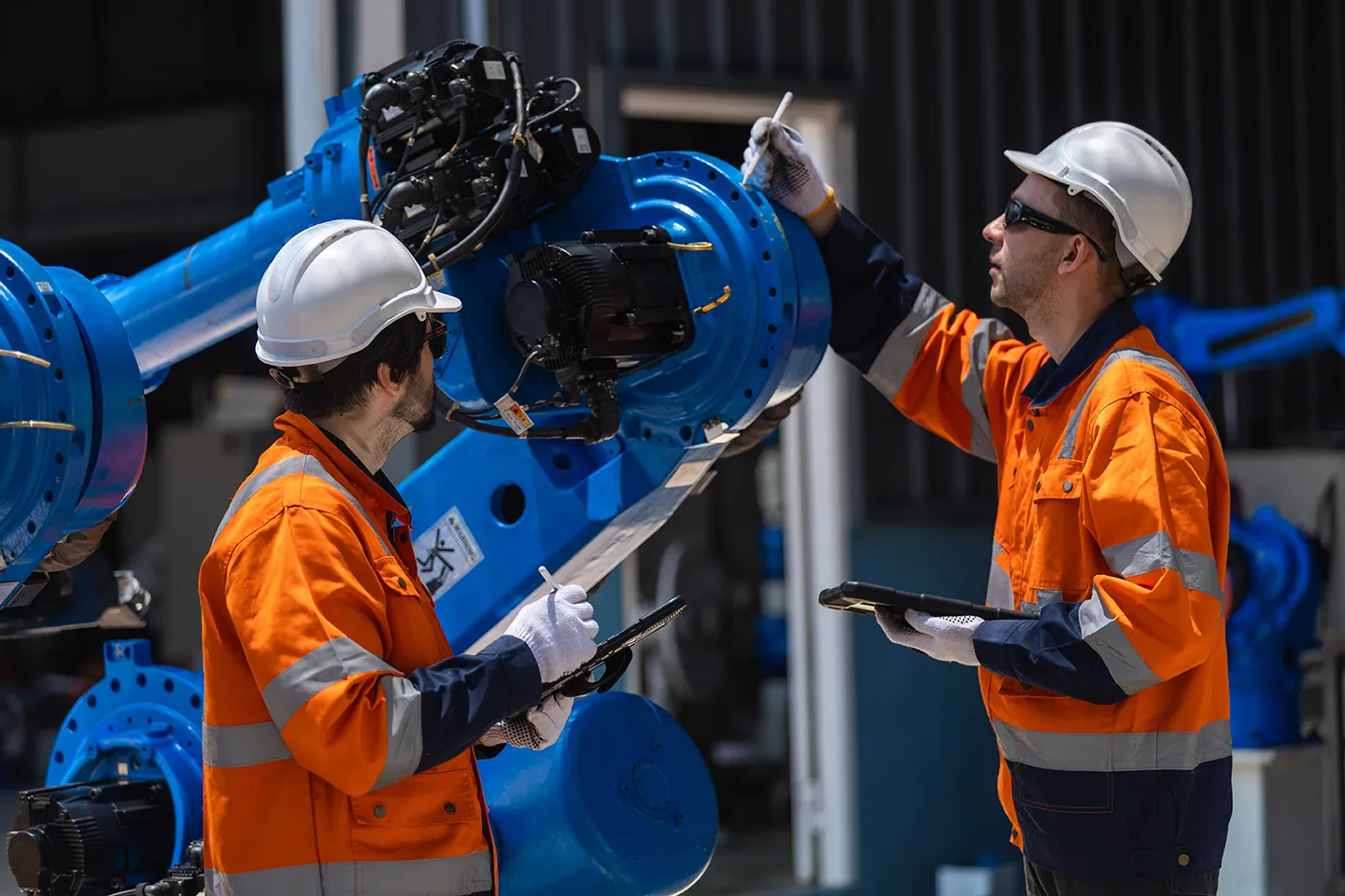 Two technicians servicing an industrial robot arm, one holding a tablet