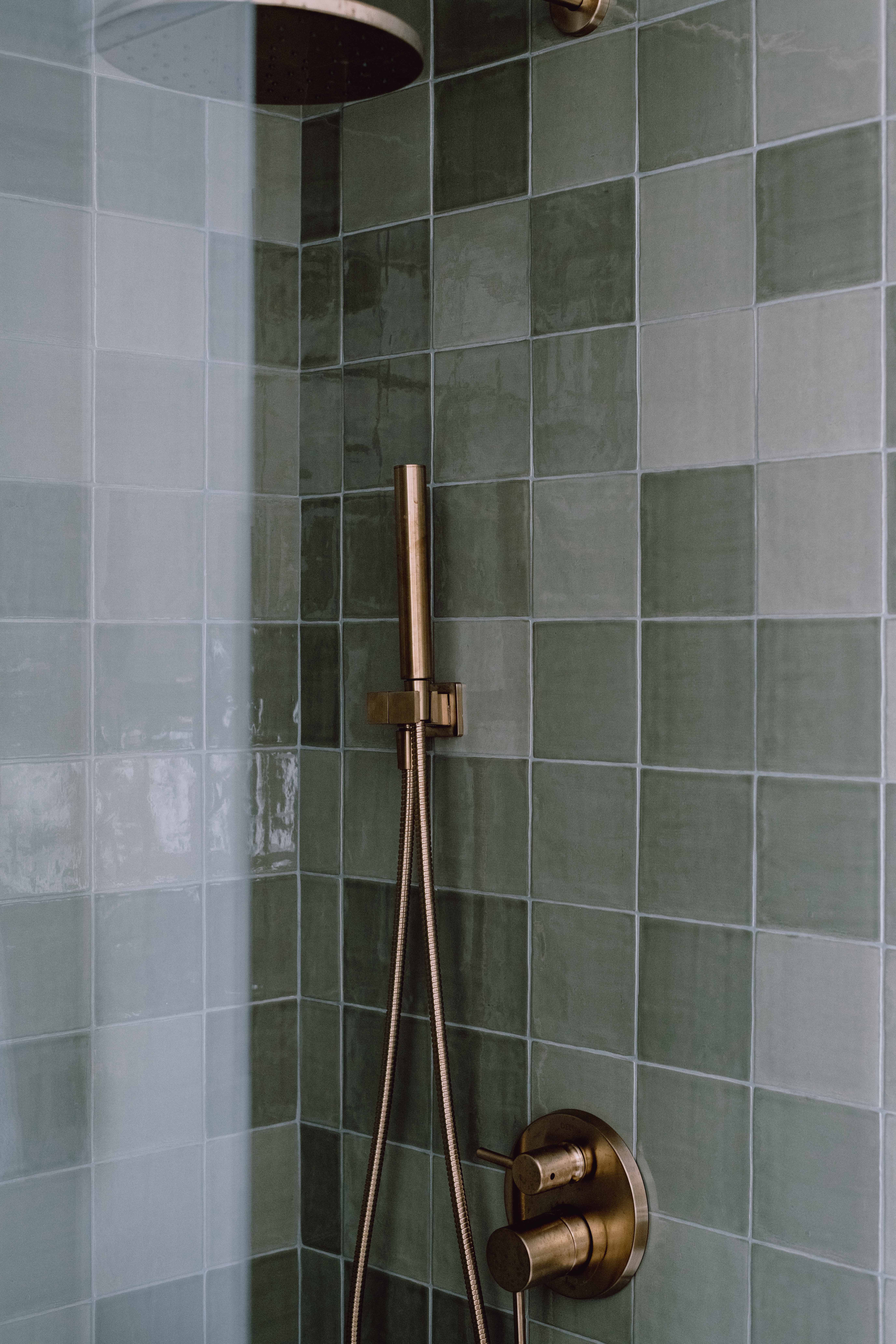A tiled shower with green tile and a rain shower head.