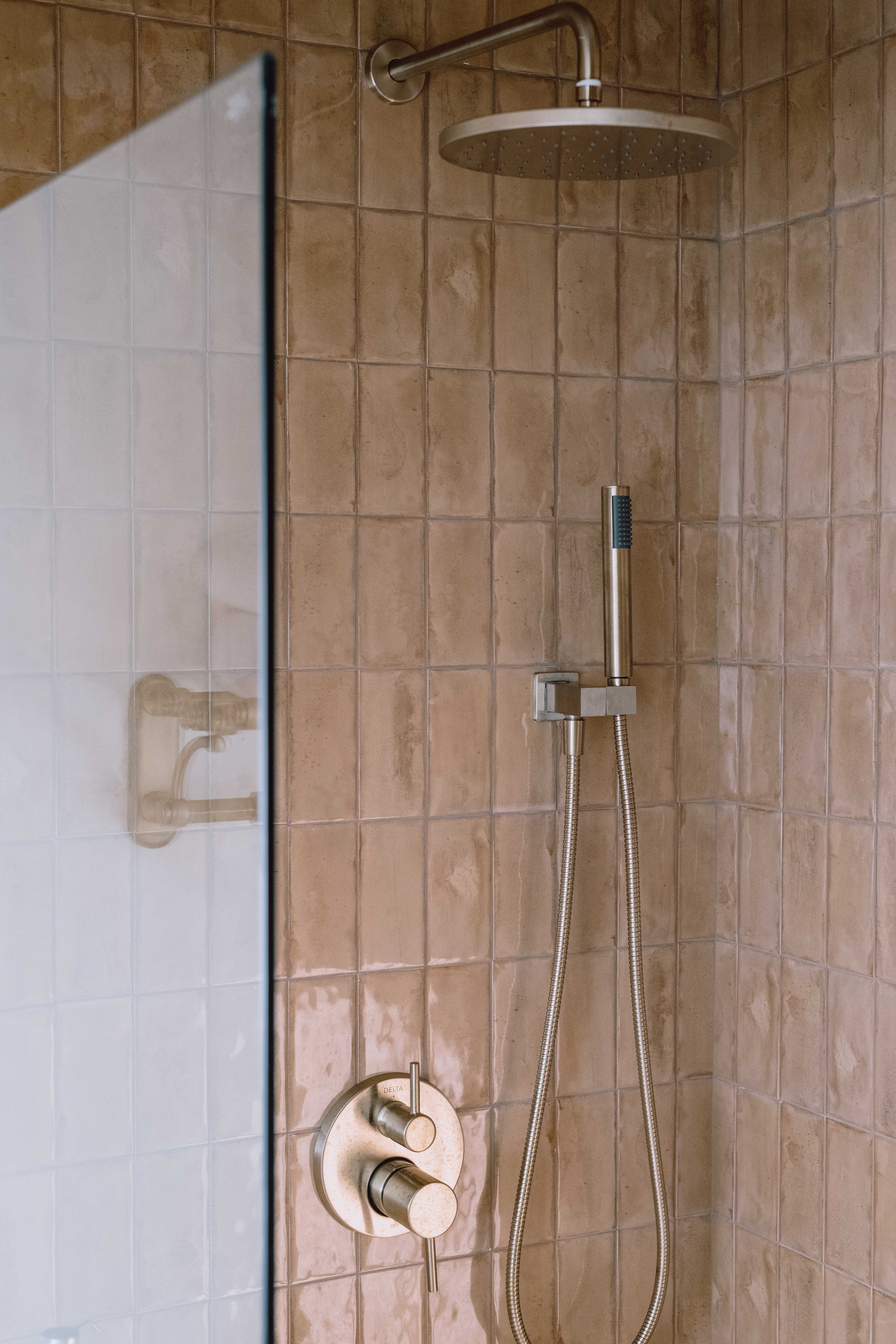 A tiled shower with brown tile and a rain shower head.